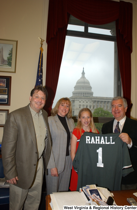 Congressman Rahall holds a "RAHALL" sports jersey and stands with a man, woman, and girl in his Washington office.