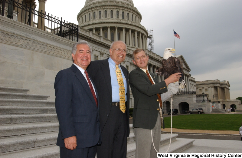 Congressman Rahall and John Dingell, Jr., stand with another man holding an eagle during a press conference in front of the Capitol Building.