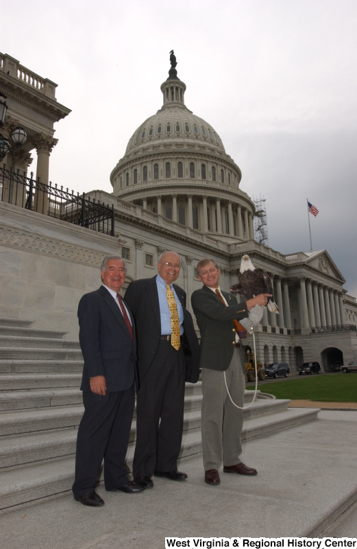 Congressman Rahall and John Dingell, Jr., stand with another man holding an eagle (facing camera) during a press conference in front of Capitol Building.