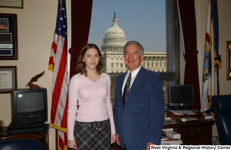 Congressman Rahall stands in his Washington office with a woman wearing a pink shirt and plaid skirt.