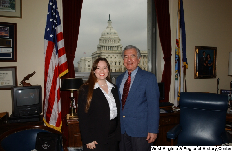 Congressman Rahall stands in his Washington office with a woman wearing a white striped blouse and black jacket.