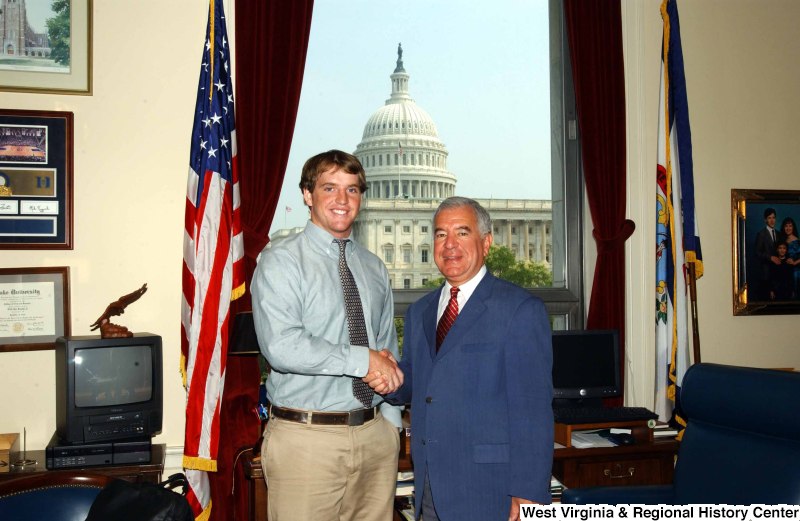 Congressman Rahall stands in his Washington office with a man wearing a blue-tinged shirt and khaki pants.