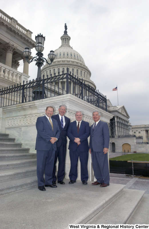 Congressman Rahall stands on the steps of the Capitol Building with three men wearing suits.