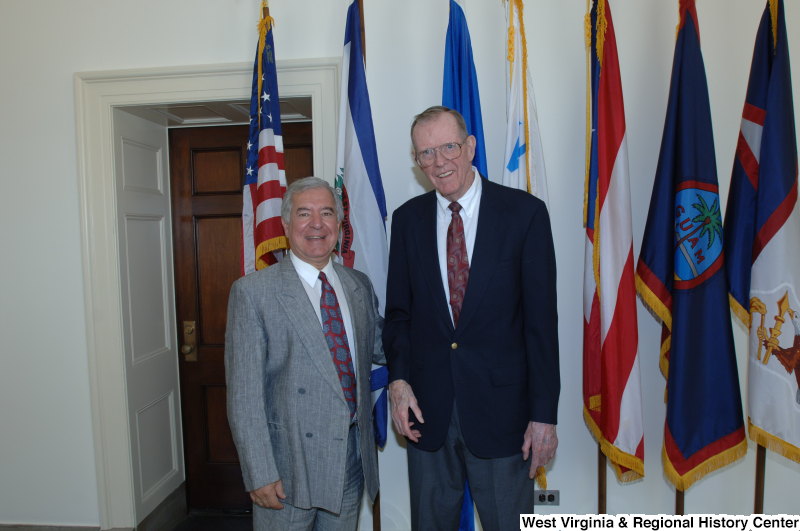 Congressman Rahall stands next to flags with a man in a blue blazer and burgundy tie.