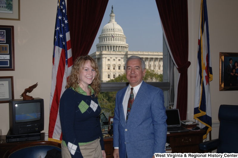Congressman Rahall stands in his Washington office with a woman wearing a green shirt and blue, green, and white sweater.