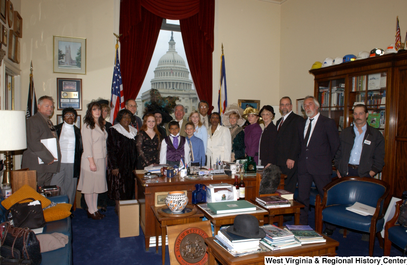 Congressman Rahall stands in his Washington office with a group of children and adults, including women wearing fancy hats.