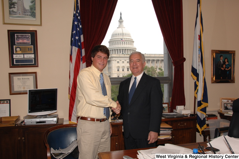 Congressman Rahall in his Washington office shakes hands with a man wearing an orange-tinged shirt.