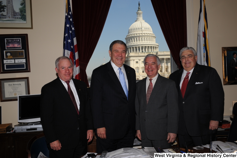 Congressman Rahall stands in his Washington office with three men wearing dark suits.