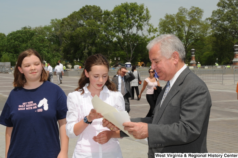 Congressman Rahall looks at papers with two girls.