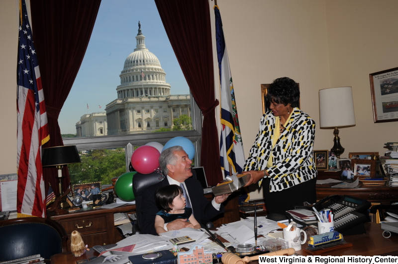 Congressman Rahall sits in his Washington office with a girl, balloons, and a woman holding a present.