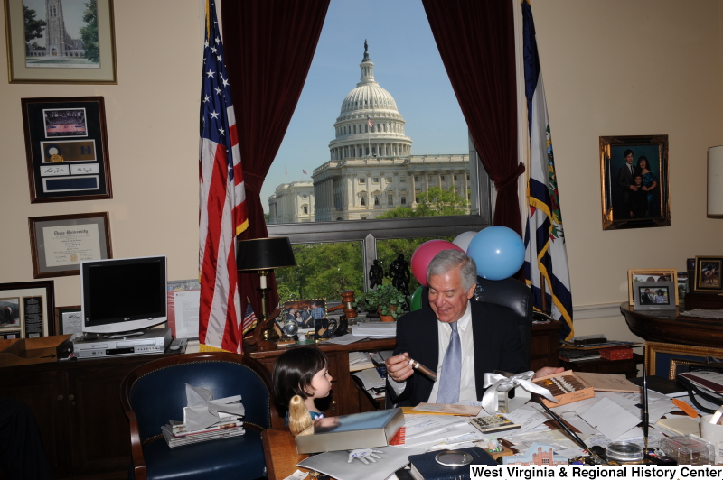 Congressman Rahall sits in his Washington office with a girl, balloons, and a cigar.