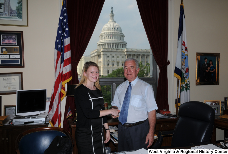 Congressman Rahall in his Washington office shakes hands with a woman wearing a black and white dress.