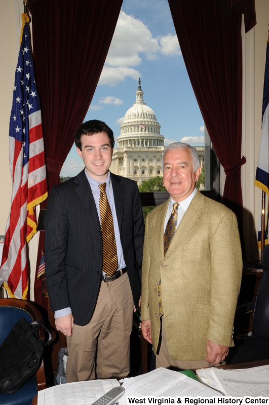 Congressman Rahall stands in his Washington office with a man wearing a dark pinstripe sport coat and gold and black striped tie.