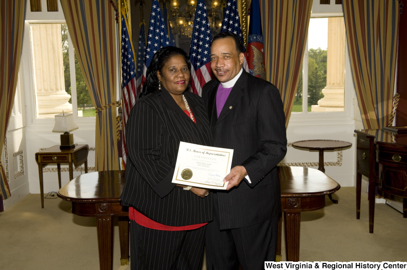 Bishop Fred T. Simms, Heart of God Ministries, Beckley, West Virginia, holds a certificate, accompanied by a woman wearing a black pinstripe suit.