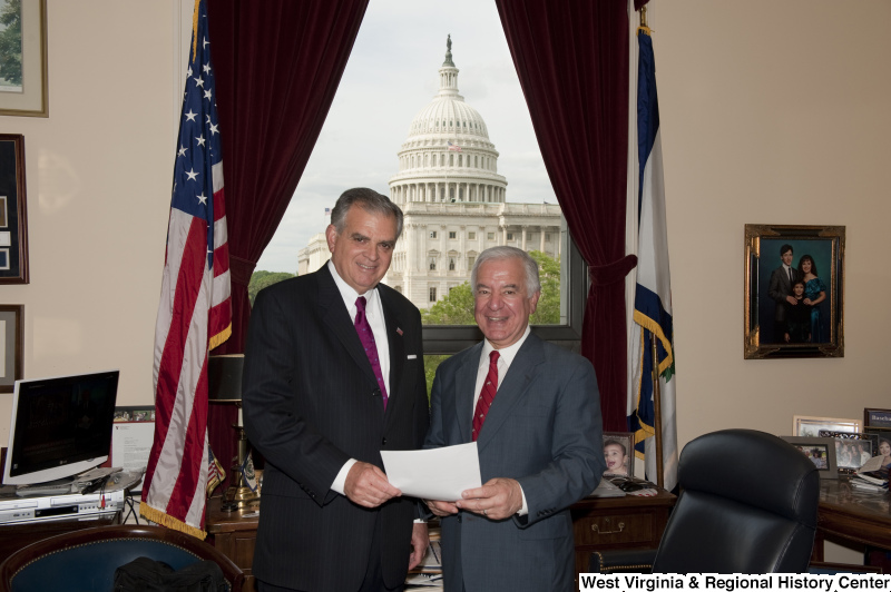 Congressman Rahall in his Washington office holds a document with a man in a dark suit and magenta tie.