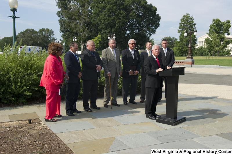 Congressman Rahall stands at a podium with seven other people during an outdoor press conference.