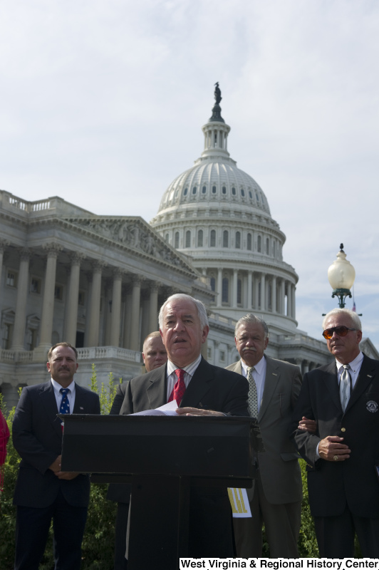 Congressman Rahall stands at a podium with other people during an outdoor press conference near the Capitol Building.