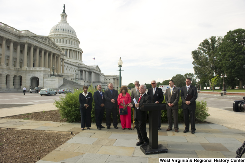 Congressman Rahall stands at a podium with eight others during an outdoor press conference near the Capitol Building.