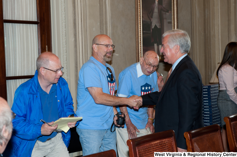 Congressman Rahall shakes hands with men wearing red, white, and blue "Honor Flight" shirts at a military award ceremony.