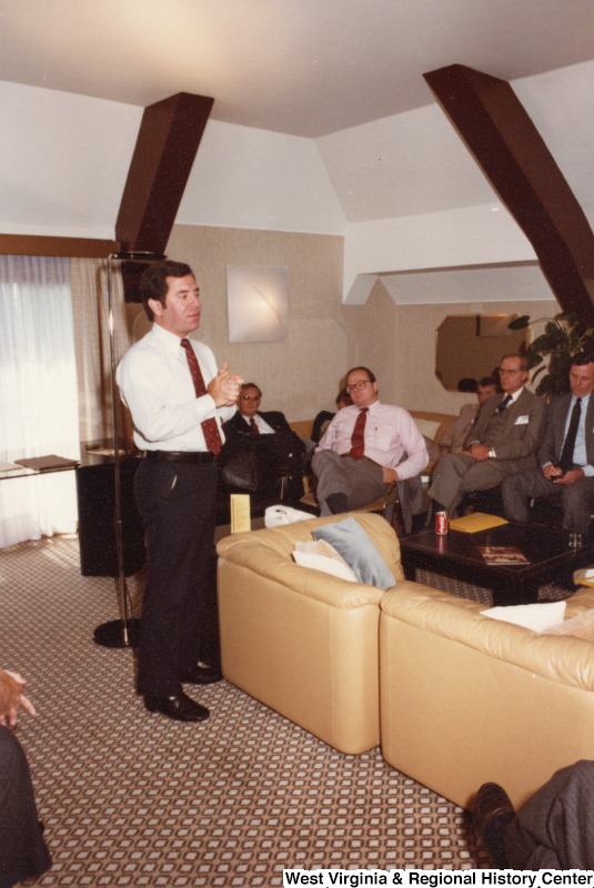 Congressman Nick Rahall II in the center of a room talking to a group of men who are sitting on couches.