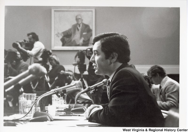 Photograph of Congressman Nick Rahall II speaking into multiple microphones. Camera men and women can be seen in the background.