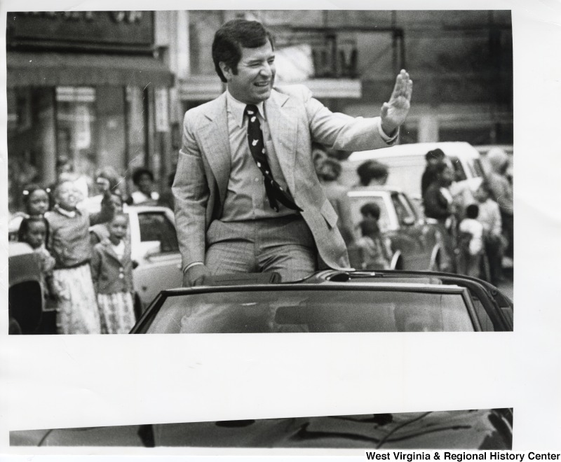 Congressman Nick Rahall II sitting in the back of a vehicle waving to the crowd during the Beckley Newspaper parade celebrating the new building.