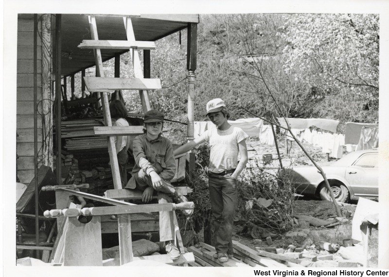 Two boys beside a flood damaged home in Mingo county. They are surrounded by debris from the flood. Another boy is behind them half hidden by a ladder.