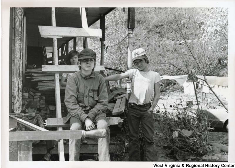 Four unidentified boys on the porch of a flood damaged home in Mingo county. One boy is sitting on a ladder leading to the second story of the house. The boys are surrounded by debris from the flood.