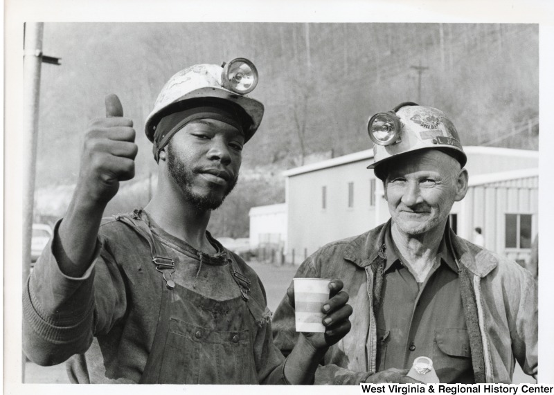 Two unidentified men wearing hard hats in Mingo county. One is giving a thumbs up and holding a disposable cup.