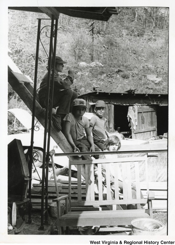 Four unidentified boys sitting on a ladder against a flood damaged home in Mingo county.