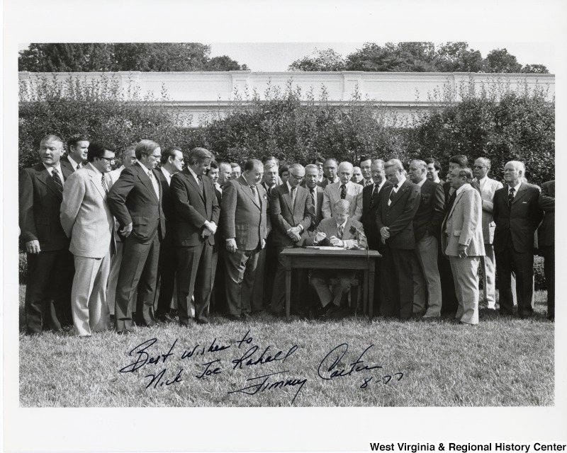 President Carter on the White House lawn signing a unknown piece of legislation. The photo is signed "Best wishes to Nick Joe Rahall. - Jimmy Carter 8-77"