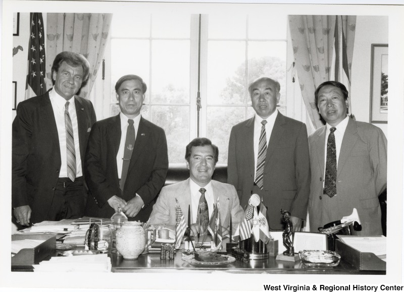 Congressman Nick Rahall II seated at his desk with four men standing beside him, two on each side. One man is Jack Fairchild, believed to be the first person on the left.