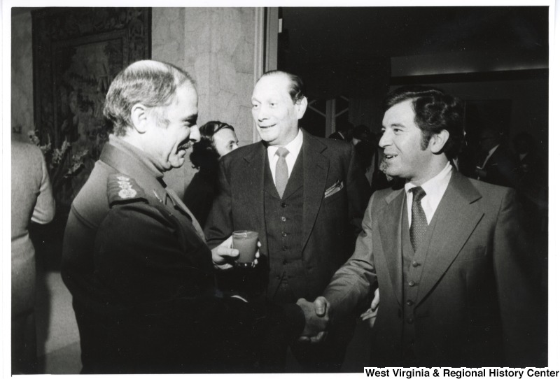 Congressman Nick Rahall II shaking the hand of the Lebanese Army Liaison. The U.S. Ambassador John Gunther Dean is standing beside Rahall. They are at the U.S. Ambassador's home.