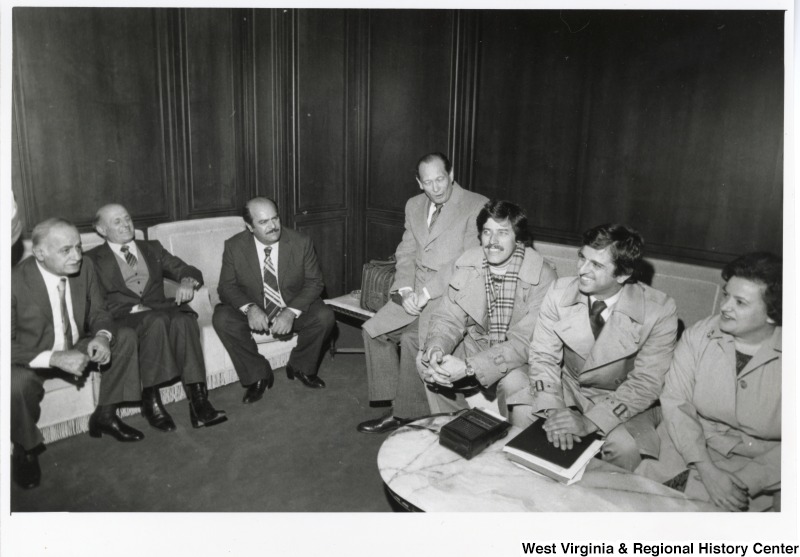 From right to left: American Ambassador John Gunther Dean, Congresswoman Mary Rose Oakar (D-OH), Congressman Toby Moffett (D-CT), and Congressman Bob Carr (D-MI). They are sitting on a couch talking to three unidentified men seated on an couch.