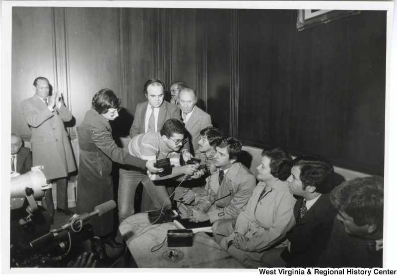 The congressmen being interviewed during a press conference upon their arrival at the Beirut International Airport. American Ambassador John Gunther Dean, their host, is standing behind the press clapping. From left to right seated: Congressman Bob Carr (D-MI), Congressman Toby Moffett (D-CT), Congresswoman Mary Rose Oakar (D-OH), Congressman Nick Rahall (D-WV), and Congressman Pete McCloskey (R-CA).