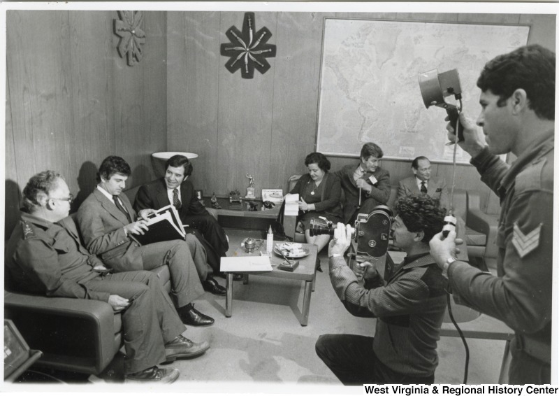 From left to right: General Khoury of the Lebanese Army, Congressman Toby Moffett, Congressman Nick Rahall, Congresswoman Mary Rose Oakar, Congressman Pete McCloskey, and Ambassador John Gunther Dean. General Khoury, Congressman Moffett and Rahall are being filmed while they talk. The meeting is taking place in General Khoury's office.