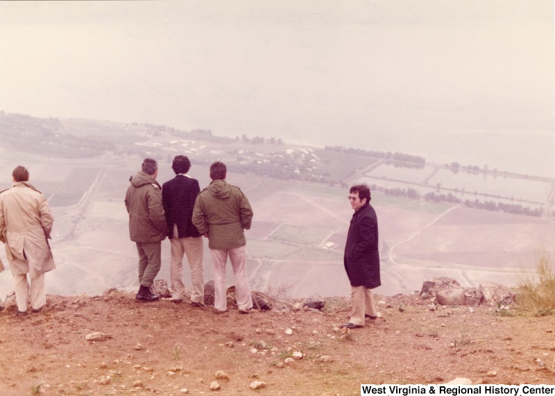 From left to right: Jim Collins, U.S. State Department escort;  Israel Army Commander; Congressman Toby Moffett; Unidentified Israel Army Aide; and Congressman Nick Rahall. They are at Golan Heights overlooking the Sea of Galilee. The photograph also notes that this is really the control point for all fighting in the Middle East.