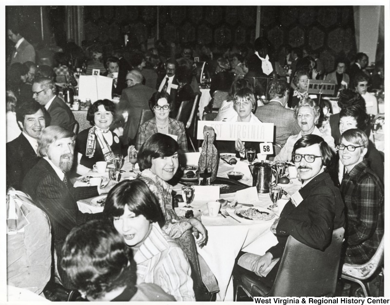 Congressman Nick Rahall II (left) and his first wife Helen, seated at a table filled with unidentified people. There is a sign saying West Virginia on the table.