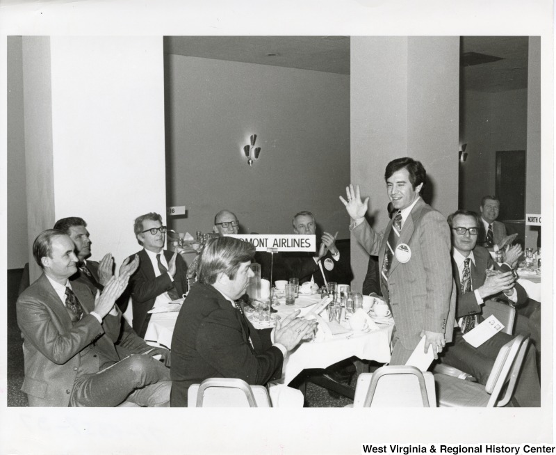 Congressman Nick Rahall II being recognized during a unidentified airline event. Rahall is sitting at a table labeled Piedmont Airlines.