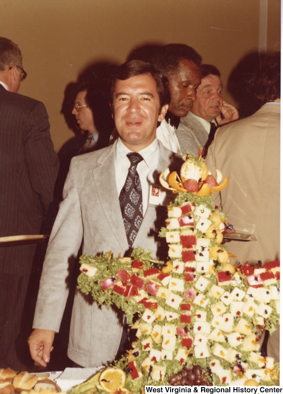Congressman Nick Rahall II standing behind a cheese and fruit sculpture.