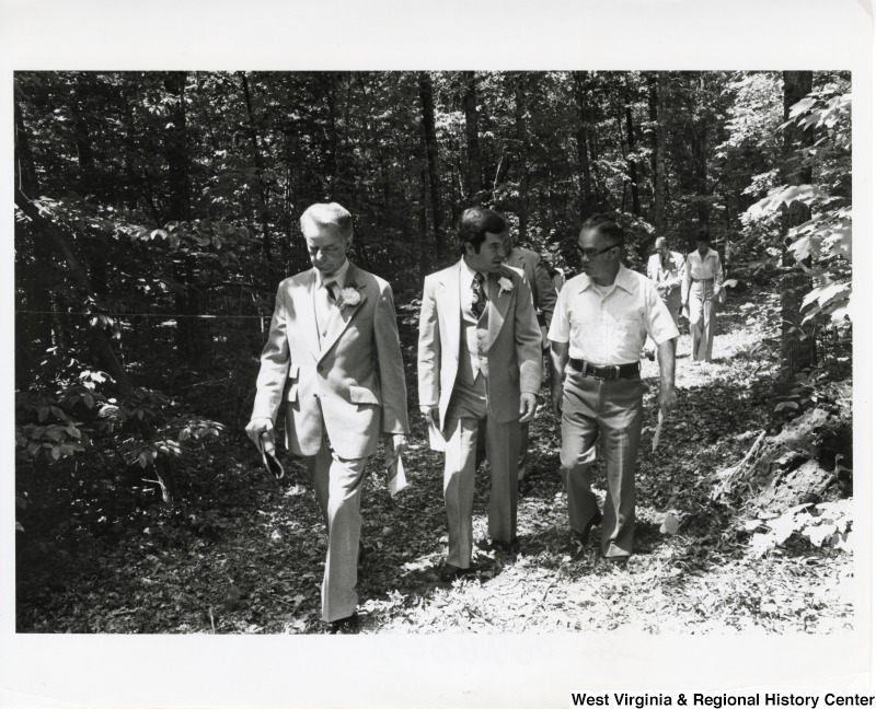 From left to right: Senator Robert C. Byrd, Congressman Nick Rahall II, and a unidentified man with the National Parks Service walking through the woods. Behind them further down the trail are two unidentified people.