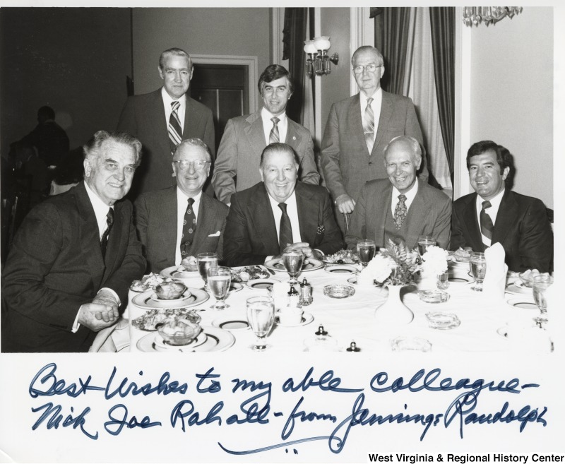 From left to right: Congressman Bob Mollohan, an unidentified man, a unidentified man, Congressman Mick Staton (middle back), Senator Jennings Randolph (seated center), an unidentified man, a unidentified man, and Congressman Nick Rahall II dinning in the Senators' Dining Room in the U.S. Capitol. The photograph is signed "Best wishes to my able colleague - Nick Joe Rahall - from Jennings Randolph."