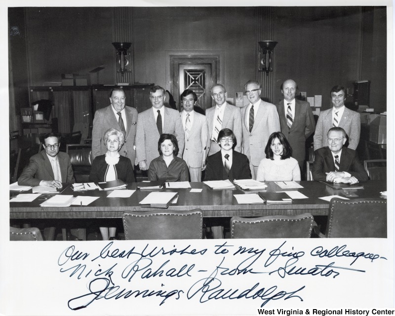 From left to right: Senator Jennings Randolph (standing); Birdie Kyle (seated, blonde), Randolph's main staffer, who later worked from Rahall; Congressman Nick Rahall (standing third from the left); Mike Fulton (fourth seated), staffer to Alan Mollohan; Mick Staton (last person standing). The rest of the people are unidentified staffers. Congressman Nick Rahall with Senator Jennings Randolph in a meeting with other staffers for the Senate Transportation Committee. Photograph is signed "Our best wishes to my fave colleague - Nick Rahall - from Senator Jennings Randolph. "