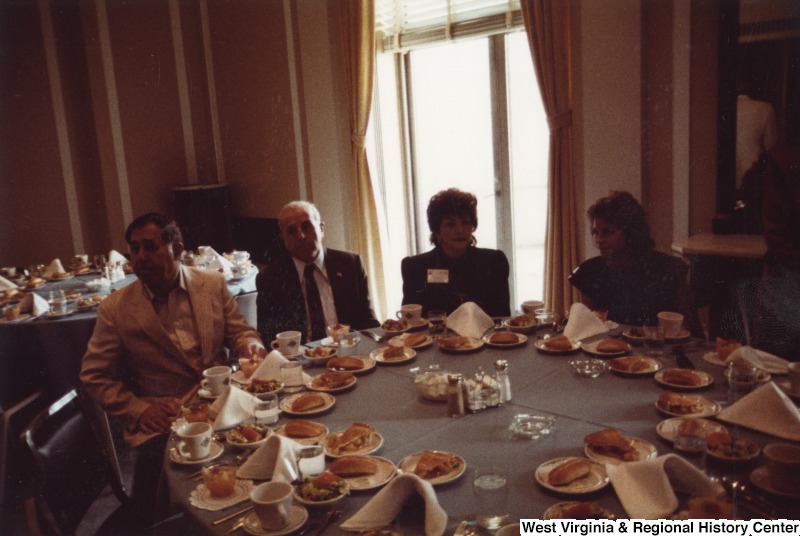 Four unidentified people seated at a table with food on it. It appears to be either breakfast or lunch.