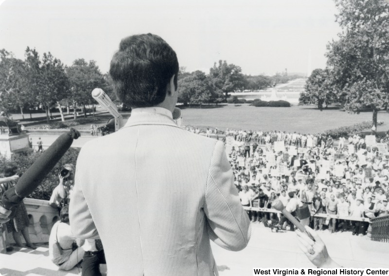 Congressman Nick Rahall II (D-WV) speaking to the press and a crowd of people. The photograph is taken from behind Rahall to give a view of the crowd.