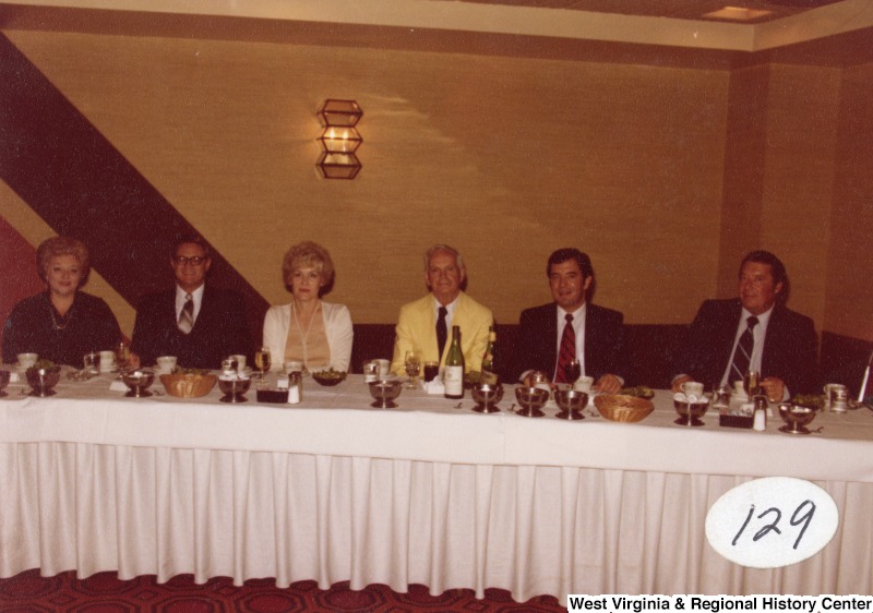 Congressman Nick Rahall II (second from the left) seated at a table with five unidentified people and a unidentified event. The photo has a sticker on it that says 129.