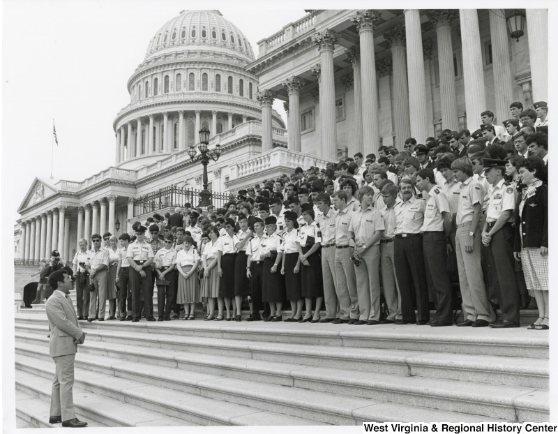 Congressman Nick Rahall II speaking to a large group of people in uniform on the Capitol steps.