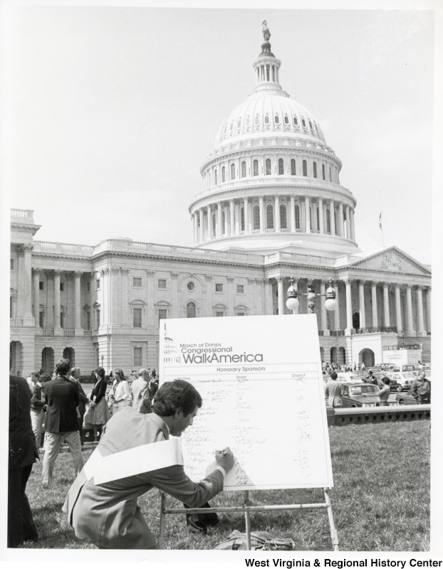 Congressman Nick Rahall II signing a board to be an honorary sponsor for the March Of Dimes Congressional WalkAmerica event. The U.S. Capitol Complex can be seen in the background.