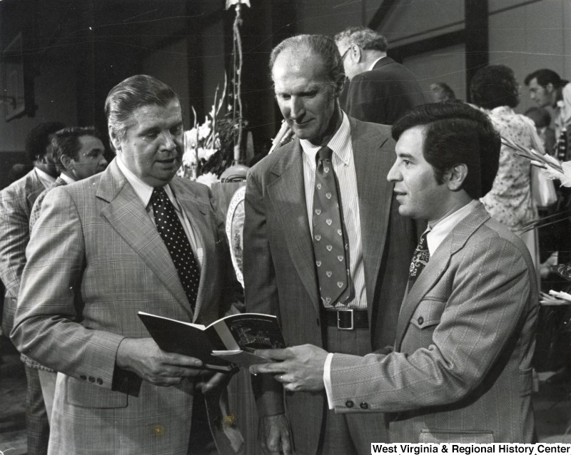 Congressman Nick Rahall II (first on the right) with two unidentified men looking at a pamphlet. Rahall is holding one side of the pamphlet.