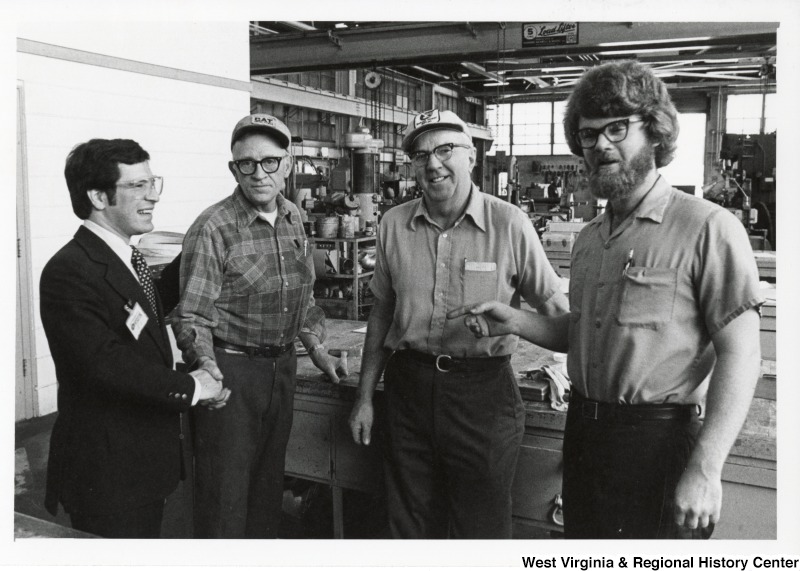 Congressman Nick Rahall II (first on the left) with three unidentified people in a shop. Rahall is shaking the hand of the man next to him.